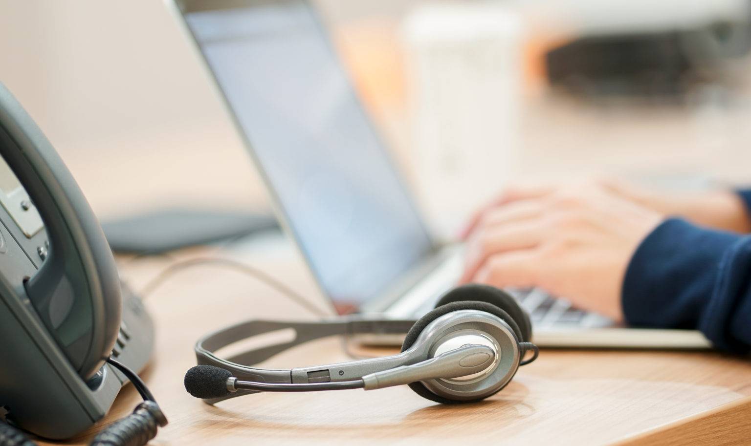 close up headset with man hand type work keyboard laptop with telephone office desk scaled